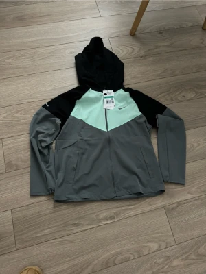 Nike miler colourblock jacka  - Nike jacka – storlek 156–170 (xs)   Snygg och funktionell Nike jacka i sportig design. Perfekt för träning, skola eller fritid. Jackan har huva, dragkedja framtill och fickor på sidorna. Färgkombination i grått, svart och mintgrönt ger en modern look. Bekväm passform och lätt material som passar bra under vår och höst.  ✅ Original Nike ✅ Storlek: 156–170 (barn/ungdom) ✅ Bra skick ✅ Perfekt för aktiv vardag  Storlek ish XS 