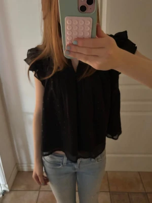 Svar - ‼️PRIS KAN DISKUTERAS‼️ STORLEK 158-164 passar mig som använder xs. Jättesöt svart blus från Gina tricot, knappt använd. Blusen har en V-uringing och volang på axlarna. Den har även lite glitter vilket man inte ser jättetydligt på bilden. 