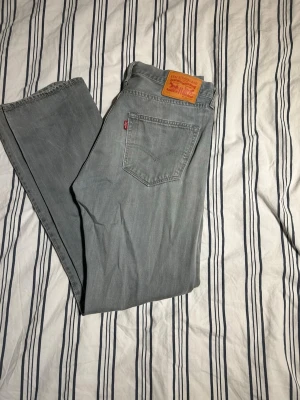Levi's 501 ljusgrå jeans W32 L32 - Säljer ett par klassiska Levi's 501 jeans i en snygg ljusgrå tvätt. Rak passform med fem fickor och knappgylf. Jeansen har den ikoniska läderpatchen bak och röd Levi's-tag på bakfickan. Perfekta till en avslappnad stil.