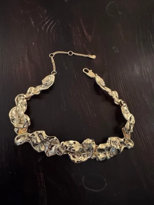 Chunky guldhalsband från Pilgrim - Säljer ett chunky statement-halsband från Pilgrim i guldtonad metall. Halsbandet har en cool, organisk och skulptural form som verkligen sticker ut. Perfekt för dig som vill ha något unikt och trendigt runt halsen. Justerbar längd med karbinhake.