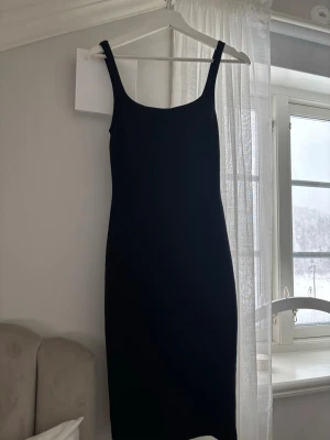 Svart långklänning  - En stilren svart långklänning med breda axelband och rak passform. Klänningen har en enkel och tidlös design som gör den lätt att styla. Perfekt för dig som gillar minimalistiska plagg.