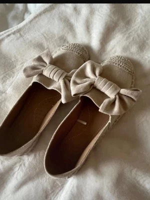 Beige ballerinaskor med rosett - Säljer dessa jättefina ballerinaskor i beige/rosa nyans med söta rosetter framtill. De är väldigt bekväma och passar perfekt till både vardag och finare tillfällen  Skorna är i bra skick, använda få gånger och utan större slitage. Innersulan är hel och rosetterna sitter fint. Enkla att matcha till klänning, jeans eller somriga outfits! 