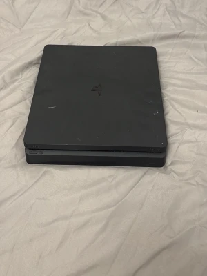 PlayStation 4 Slim - Sony PlayStation 4 Slim i svart färg. Konsolen är i gott skick med några mindre ytliga repor och märken på ovansidan. Perfekt för gaming och multimedia. En kompakt och tyst spelkonsol som passar alla PlayStation-fans.