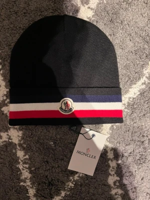 M-mössa - En snygg mössa ifrån M i färgen svart med röda och vita sträck som går runt mössan