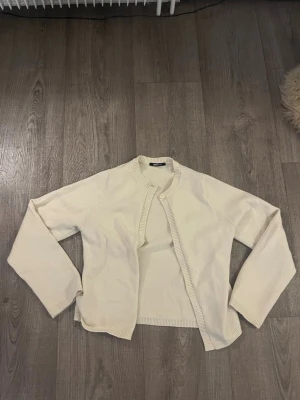 Beige calssic kofta från Gina Tricot - En enkel och stilren beige kofta från Gina Tricot i mjukt stickat material. Koftan har rund halsringning, ribbade muddar och en knapp upptill. Perfekt att slänga över en topp för en clean look.