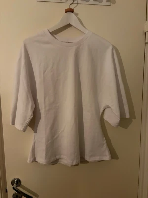 Vit figursydd t-shirt med trekvartsärm - Enkel och clean vit t-shirt med trekvartsärm och figursydd passform. Tillverkad i mjuk bomull med rund halsringning. Perfekt för dig som gillar en avslappnad och stilren vibe.