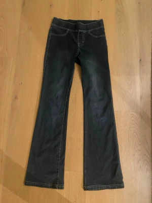 Bootcut jeans med rosetter från H&M - Mörkblå bootcut jeans från H&M i storlek 152. Byxorna har vita kontrastsömmar och söta rosetter på bakfickorna. Tillverkade i mjukt bomullsmaterial med fejk fickor på framsidan och bekväm midja.