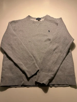 Grå sweatshirt från Polo Ralph Lauren S - Klassisk grå sweatshirt från Polo Ralph Lauren i storlek XL. Tröjan har rund halsringning, långa ärmar och den ikoniska broderade loggan på bröstet. Tillverkad i mjuk bomull för skön vardagsstil.