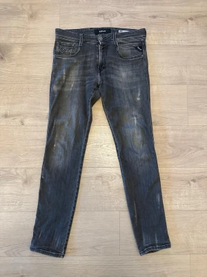 Replay Anbass Slim Fit Jeans, grå - Säljer ett par Replay Anbass slim fit jeans i tvättad grå färg med snygga slitningar. Klassisk femficksmodell med dragkedjegylf och Replay-logga på fickan. Jeansen har smal passform och raka ben, perfekta till sneakers eller boots.