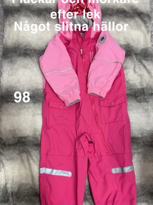 Rosa skaloverall Polarn O. Pyret stl 98 - Säljer en rosa skaloverall från Polarn O. Pyret i storlek 98. Overallen har två nyanser av rosa, reflexdetaljer på ben och ärmar, huva och dragkedja framtill. Materialet är tåligt och overallen har praktiska fickor med knappar.🌸 Använd två gånger eftersom vi har haft skalset som använts istället. Fläckar och mörkare efter lek. Var namnad med lapp men bottagen. Något slitna hällor. Storlek 98. 