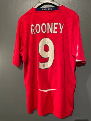 England Rooney #9 – Original Umbro landslagströja (2008–2010) - Säljer en ikonisk England bortatröja med Wayne Rooney #9 – en riktig klassiker från Umbro-eran. Äkta original, inga repliker.  🔹 Spelare: Wayne Rooney 🔹 Nummer: 9 🔹 Lag: England 🔹 Tillverkare: Umbro 🔹 Period: ca 2008–2010 🔹 Storlek: L 🔹 Skick: Bra vintage-skick med naturlig patina på trycket – ger rätt retro känsla  Perfekt för samlare, fotbollsnördar eller som statement-piece i vardagsfitten. Rooney i landslaget är odödlig 🏴  Skickas snabbt! Hör av dig vid frågor!