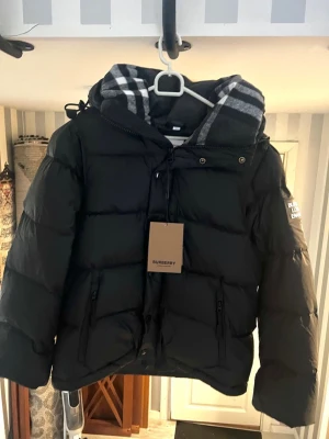 Burberry pufferjacka - Tjenare! Jag gör mig av med min Burberry-jacka eftersom den inte riktigt passar in i min garderob längre. Den är i toppskick, nästan oanvänd och helt felfri. Jag köpte den online och den är givetvis äkta. En smart detalj är att man kan ta av ärmarna och använda den som väst. Perfekt för både höstkyliga dagar och som varmt lager under vintern. Fråga på om det är något du undrar! 👍