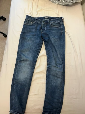Jack & Jones Slim Glenn jeans blå - Snygga blå jeans från Jack & Jones, modell Slim Glenn. De har en slim passform, klassisk femficksdesign och är tillverkade i mjukt jeanstyg. Färgen är mörkblå med lätt slitningar och kontrastsömmar. Perfekt för dig som gillar en smal siluett och stilren look.