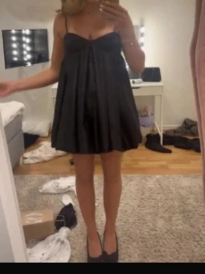 Svart klänning - Supersöt svart kort babydollklänning med tunna axelband och vidd i kjolen. Klänningen har en luftig och flowy passform som ger en avslappnad men ändå chic vibe. Perfekt för dig som gillar en enkel men ändå trendig look. 