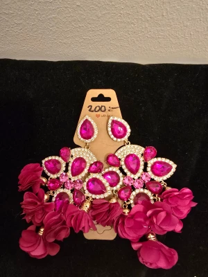 Glittrande örhängen  - Bilden visar ett par stora örhängen med rosa stenar och blommor, ingen väst finns på bilden.