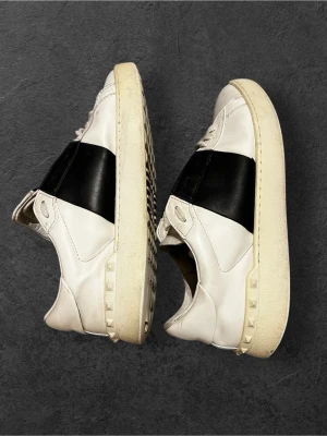 Valentino Garavani Open sneakers vit/svart - Säljer ett par Valentino Garavani Open sneakers i vitt skinn med bred svart läderdetalj över mitten. Klassisk rund tå, platt sula med nitar längs kanten och vita snören. Med originalkartong och dustbag. Skicket på dem är 7.5/10! Perfekt nu till vintern! 