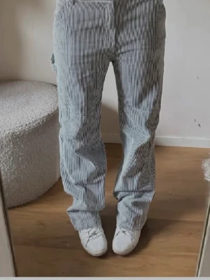 Randiga blåvita jeans  - Säljer ett par snygga cargopants med blåvita vertikala ränder. Byxorna har raka ben, praktiska fickor på sidorna och är tillverkade i ett mjukt bomullsmaterial. Perfekt för dig som gillar en chill och stilren look.