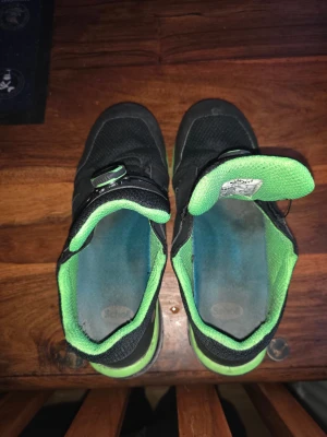 Svarta sneakers med gröna detaljer - Scholl sneakers i svart med gröna inslag och detaljer. Ovandel i mesh och syntet, med smart snörningssystem via BOA-vred för enkel justering. Platt sula med slitstarkt mönster, rund tå och bekväm stoppning. Perfekt för dig som gillar sportig stil och funktion.