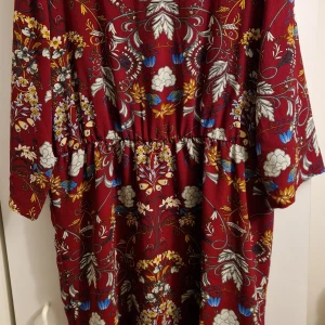 Vinröd blommig kortklänning - Vinröd knälångtklänning med blommönster. Klänningen har resår i midjan.