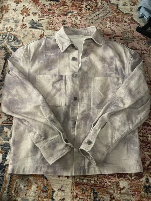 Overshirt i ljusgrått från Zara - Säljer en snygg overshirt från Zara i storlek S. Jackan har ett unikt ljusgrått och beige mönster, två stora bröstfickor och knappar framtill. Perfekt att slänga över en hoodie eller t-shirt för en chill look.