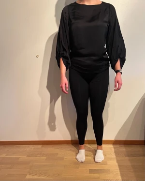 Svart, ”silkig” topp med detaljer vid armarna. Kappahl  - Tvättråd: 30°