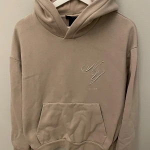 Beige hoodie från H&M loose fit - Säljer en beige hoodie från H&M i loose fit med broderad text 'NY' på bröstet. Tröjan har huva, känguruficka och mjukt material som känns skönt mot huden. Perfekt för chill dagar och enkel att matcha med jeans eller joggers. (Passar även M!)
