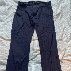 Mörkblå golfbyxor Peak Performance - Snygga mörkblå golfbyxor från Peak Performance med klassisk rak passform och diskreta fickor både fram och bak. Byxorna har bälteshällor och är tillverkade i ett mjukt, lätt material som ger en stilren look. Perfekta för dig som gillar enkel och clean stil.