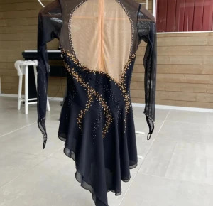 Svart konståknings klänning med guldiga detaljer💕 - Klänningen har öppen rygg, långa ärmar, asymmetrisk nederdel och är dekorerad med guldiga och svarta paljetter i vågiga mönster. Materialet är lätt och följsamt, perfekt för dans eller scenframträdanden.