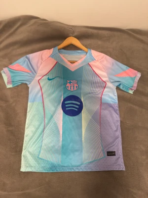 FC barcelona fotbollströja - Säljer en FC Barcelona fotbollströja från Nike i pastellfärger med coolt grafiskt mönster. Tröjan har korta ärmar, V-ringad krage och är tillverkad i lätt polyester. Färgerna går i ljusblått, rosa och lila med klubbmärke och Spotify-logga på bröstet. PRIS KAN DISKUTERAS