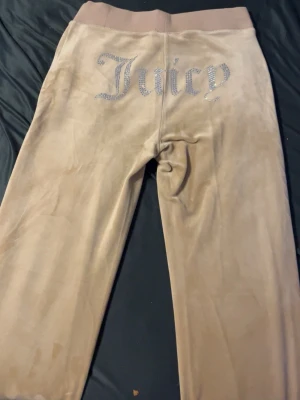 Beiga velourbyxor Juicy Couture XS - Supermjuka beiga velourbyxor från Juicy Couture i storlek XS. Klassisk Juicy-logga i strass på baksidan, bred resår och snörning i midjan. Perfekta för en chill och trendig look.