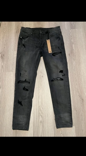 Svarta jeans från Ksubi med tryck - Svarta jeans från Ksubi med slitna detaljer och tryck på bakfickan. Modellen har raka ben, knappgylf med Ksubi-logga och coolt statement-tryck 'Royalty Heroism And The Streets' på bakfickan. Jeansen har klassisk femficksdesign och är gjorda i jeansmaterial.