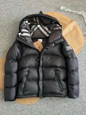 Svart pufferjacka Burberry  - Svart pufferjacka från Burberry med avtagbara ärmar så du kan bära den som väst. Jackan har dragkedja, knappar och två fickor med dragkedja. Insidan av huvan har klassiskt rutigt Burberry-mönster i grått, vitt och rött. Perfekt för kalla dagar och riktigt snygg streetstil.