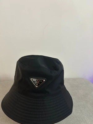 Svart bucket hat från Prada - Säljer min svarta Prada bucket hat. Den är i väldigt fint skick, bara använd 2–3 gånger. Sitter bra, inga skador eller något. Äkta vara. Kan mötas upp i [stad] eller skickas. 