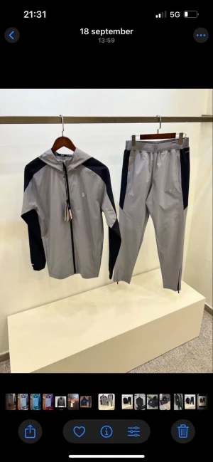 Grå vindjacka från Under Armour - Snygg grå vindjacka från Under Armour med svarta paneler på ärmar och axlar. Jackan har huva, hel dragkedja framtill och sportig design. Perfekt för träning eller chill. Materialet är lätt och syntetiskt för maximal komfort.