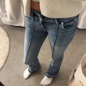 Blå bootcut jeans från Bershka - Snygga blå jeans från Bershka i bootcut-modell med låg midja. Jeansen har klassisk femficksdesign, markerad söm längs benen och är tillverkade i mjukt denimtyg. Perfekt för dig som gillar en retro vibe och vill ha ett par jeans med lite utsvängda ben.