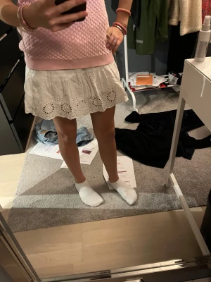 Vit kort kjol med broderade detaljer - Supersöt vit kort kjol med volang och broderade blommor längs nederkanten. Kjolen har en luftig passform och är gjord i bomull, perfekt för varma dagar. Elastisk midja för extra komfort och snygg passform. Pris kan diskuteras