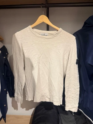 Vit långärmad tröja Stone Island - Beige/vit långärmad tröja från Stone Island med ikonisk patch på ärmen. Tröjan är stickad i bomull och har en clean, stilren look som passar perfekt till jeans eller cargobyxor.