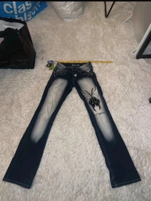 Blå Young Age jeans Y2K  - Midjemått: 30/32 cm stretchiga.       innerbandslängd: 83 cm.                                                        blå jeans från Young Age med broderat fjärilsmotiv på ena benet och detaljerade broderier samt nitar på bakfickorna. Jeansen är låg midjade, flare och slitna effekter framtill och baktill.  Pris kan diskuteras! 