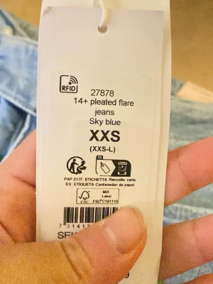 Sky blue pleated flare jeans XXS Gina 14+ - Säljer ett par ljusblå jeans med flare och pressveck, i modellen 'pleated flare jeans'. Jeansen har slitna detaljer, stora fickor fram och bak samt dubbla knappar i midjan. Perfekt för dig som gillar en trendig och retro vibe.