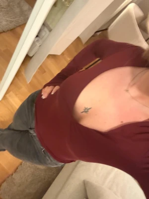 Vinröd långärmad topp med v-ringning - Säljer en vinröd långärmad topp med djup v-ringning. Modellen är slim och sitter snyggt mot kroppen. Tunn och mjuk, perfekt att styla med jeans eller kjol. Färgen är mörkt vinröd och materialet känns som bomull eller polyester.