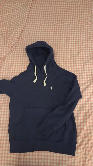 BLÅ RL-HOODIE - Marinblå hoodie från Polo Ralph Lauren Klassisk och stilren hoodie i marinblått med vit dragsko och broderad Polo-logga på bröstet. Mjuk, varm och perfekt för både vardag och chill-dagar.