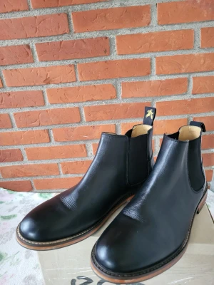 Nästan nya! Lyle & Scott Chelsea Boots, Svart, EUR 42 - Ett par klassiska Chelsea boots från Lyle & Scott. Skorna är i bra skick och har resår på sidorna för enkel på- och avtagning. Nästan nya och perfekt för både vardag och fest.
