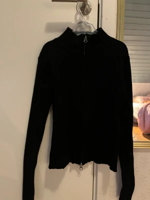 Svart ribbad kofta från H&M - Svart ribbad kofta från H&M med lång ärm och hel dragkedja framtill. Tröjan har en lite högre krage och är tillverkad i mjukt stickat material.  Sälja då jag inte tkr att den passar min stil längre och är lite kort för mig💕