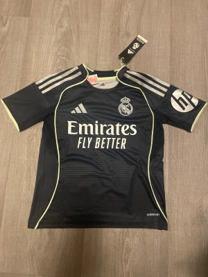 Real Madrid Borta Tröja 25/26 - Real Madrid borta tröja 25/26 Helt ny, bilder tagna direkt ur påsen. Storlek 140 Kids 9-10. Nypris 1200kr.
