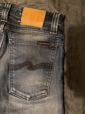 Nudie jeans - Snygga blå jeans från Nudie Jeans i modellen skinny med klassisk femficksdesign och coola slitningar. Jeansen har en mörk tvätt med ljusare partier och Nudie Jeans logga på bakfickan samt läderpatch i midjan. Perfekt passform och stilren look. Jeansen passar dig som är runt 163-173. Hör av dig om du har några frågor. Priset är prutbart via enkel affär