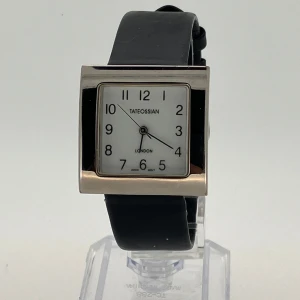 Snygg  Tateossian London damklocka  - Elegant klocka från Tateossian London med en fyrkantig urtavla i silver och svart  läder armband. Urtavlan har tydliga svarta siffror och visare mot en vit bakgrund. Perfekt för en stilren look. Klockan har ny batteri och fungerar perfekt.  