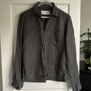Grå skjorta från A Day's March - Stilren grå skjorta från A Day's March i storlek medium(sitter S). Skjortan har klassisk krage, bröstficka och knäppning framtill. Perfekt för dig som gillar en enkel och tidlös look.