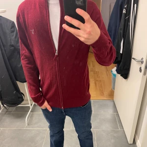 Vinröd kofta från GANT med dragkedja - Säljer en vinröd kofta från GANT med hel dragkedja och diskret logga på bröstet. Tröjan är stickad i mjukt material och har ribbade muddar vid ärmslut och nederkant. Perfekt för lager-på-lager och snygg till jeans. Skick 9/10 med en liten missfärning