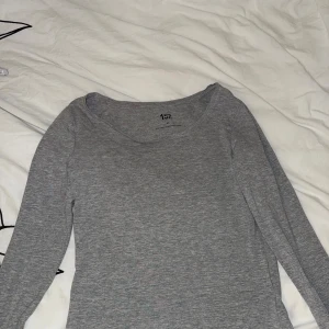 Grå långärmad topp från 157 - Slimmad grå långärmad topp från 157 med rundad halsringning. Mjuk och stretchig bomullsmix som sitter tajt mot kroppen och passar perfekt till jeans eller kjol. Enkel och stilren design som funkar året runt.