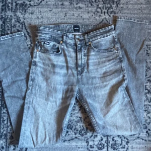 Grå jeans från BOSS - Snygga grå jeans från BOSS med klassisk femficksdesign och silverfärgade nitar. Jeansen har en rak passform och normal midja, med BOSS-logga på både fram- och bakficka. Perfekt för dig som gillar stilrena och tidlösa jeans. I slim. Ny pris ca 1000 kr mitt pris 500kr! Tveka inte att höra av dig om fler frågor. 